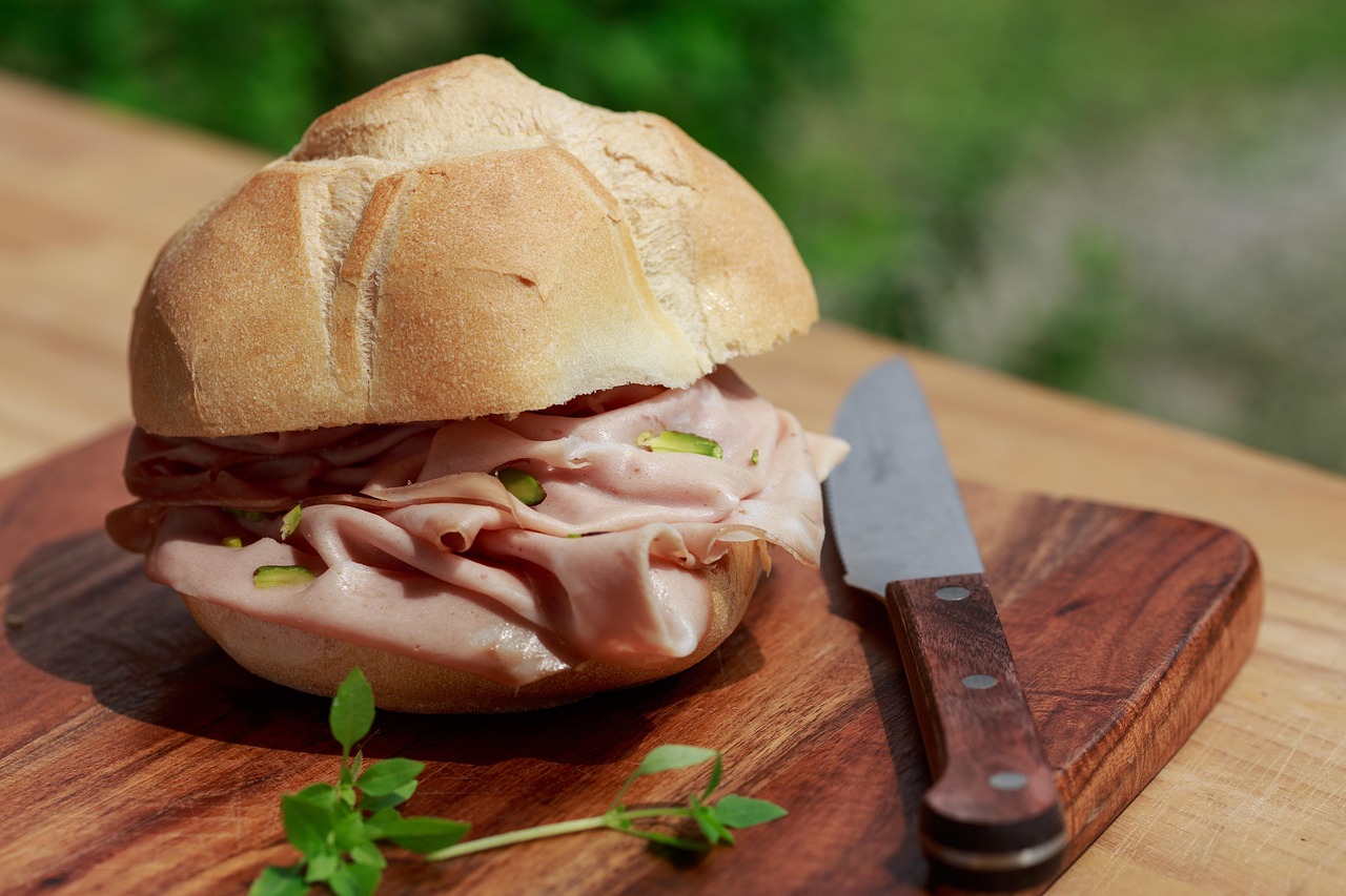 Immagine di una fetta di mortadella su un tagliere di legno con verdure fresche sullo sfondo.