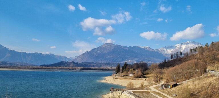 Vista panoramica del lago nascosto in Friuli, circondato da montagne e vegetazione.