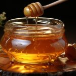 Barattolo di miele con etichetta, posizionato su un tavolo di legno, accanto a un cucchiaino di legno.