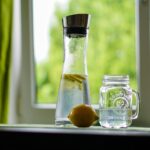Donna che beve un bicchiere d'acqua al risveglio, simbolo di benessere e idratazione.